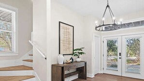 Un escalier menant à un palier où se trouvent une console, un lustre et une porte à panneaux de verre.
