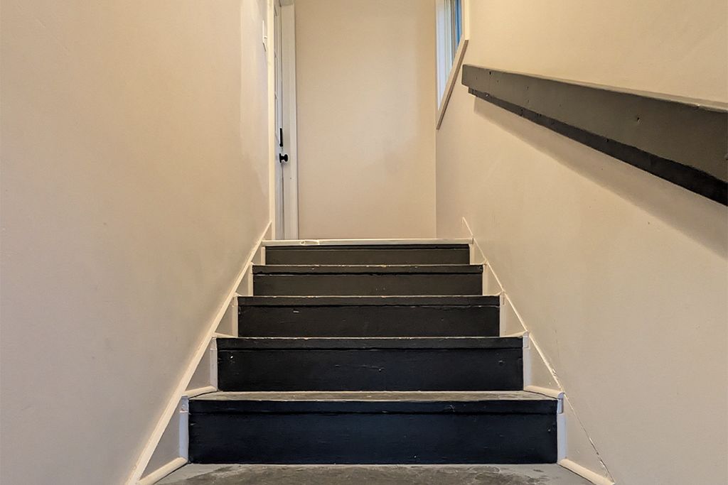A staircase with a handrail on the right side, leading to an open door at the top.