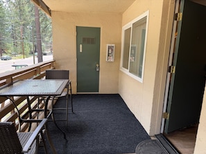 A covered outdoor seating area with a table and chairs, a door with a window, and a view of the street. - CYC0605 - Herbert Hideaway (South Lake Tahoe)