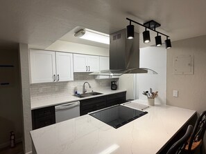 A modern kitchen with white cabinets, a black stove, and pendant lighting. - CYC0605 - Herbert Hideaway (South Lake Tahoe)