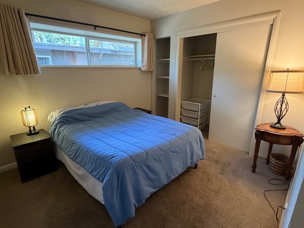 Un dormitorio con cama, mesita de noche, lámpara, armario y ventana.