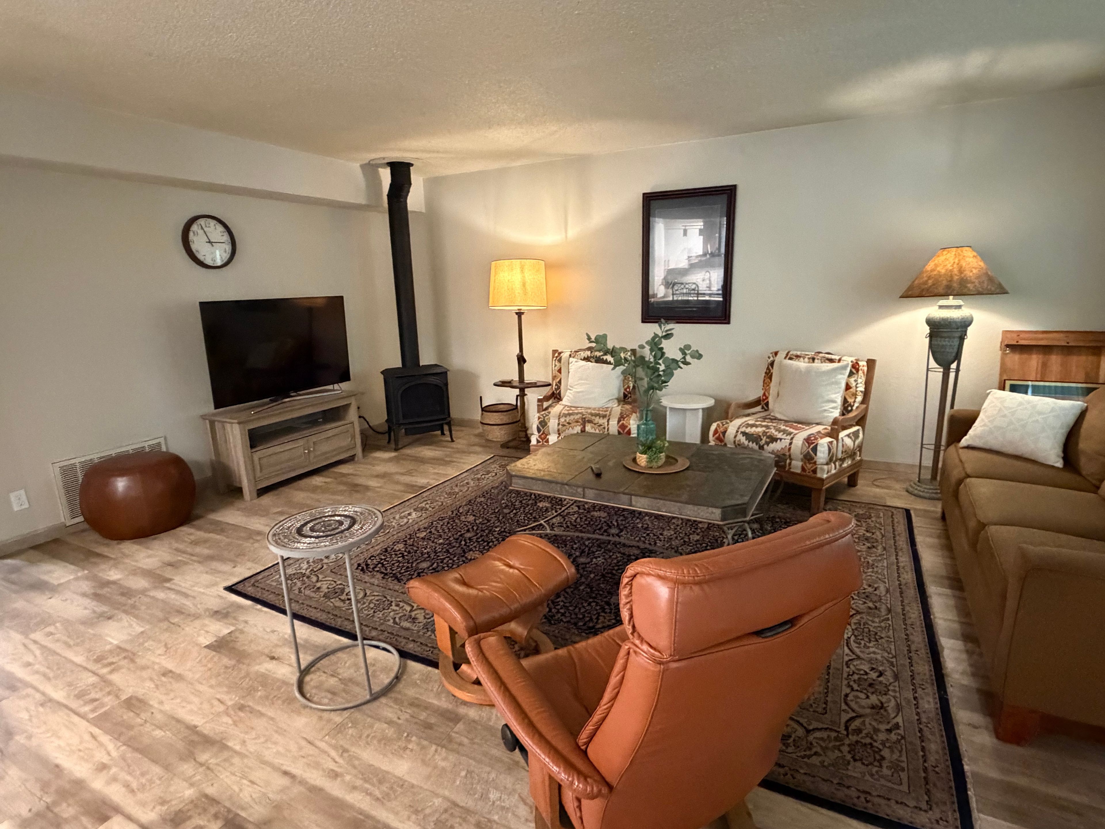 A living room with a sofa, armchair, coffee table, TV, fireplace, and lamps.