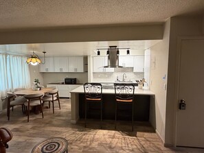Cocina compacta con armarios blancos, una isla central y un comedor con mesa y sillas.