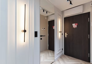 Un pasillo con un accesorio de iluminación, una puerta con un cartel y un equipo de aire acondicionado.
