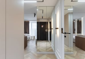 Una habitación de hotel moderna con un armario con espejo, una cama, una mesita de noche y un baño visible a través de las puertas del armario.