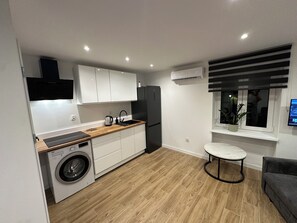 A compact kitchen with a washing machine, a sink, a refrigerator, and a small dining area with a table and a couch.