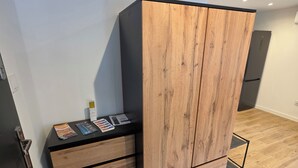 Una habitación moderna con un armario de madera, un escritorio pequeño negro con revistas y suelo de baldosas.