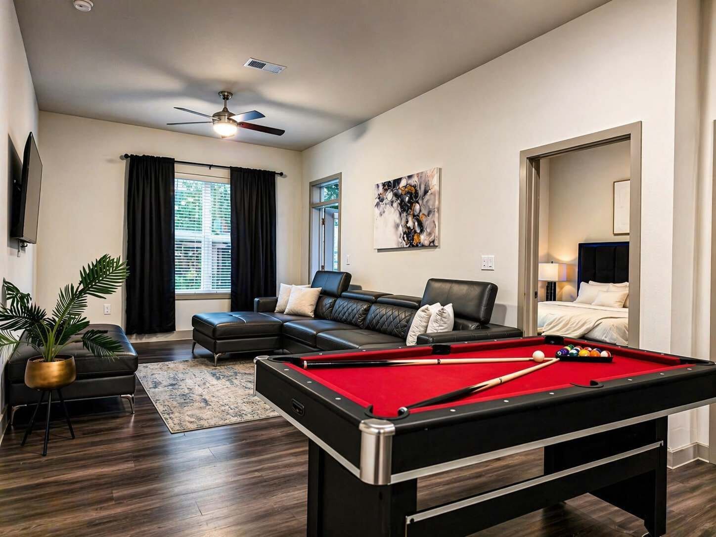 Ein modernes Wohnzimmer mit Poolbillard, einer Couch, einem Deckenventilator und einem großen Fenster mit Vorhängen.