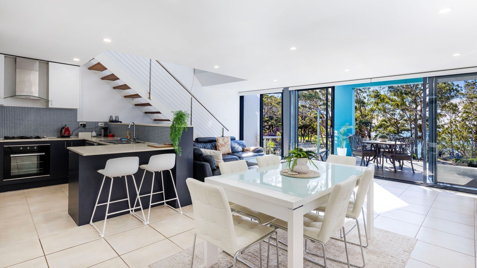 A modern kitchen with a central island, bar stools, and a dining area with a glass table and chairs.