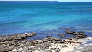 A rocky shoreline with clear blue water and a distant landmass. - Bruma on Bowen - Opposite Shark Net Beach (Huskisson)
