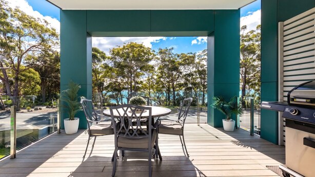 An outdoor patio with a round table and chairs, a grill, and potted plants. - Bruma on Bowen - Opposite Shark Net Beach (Huskisson)
