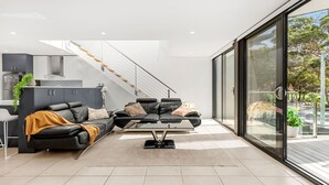A modern living room with a sofa set, a coffee table, and a staircase leading to an upper level. - Bruma on Bowen - Opposite Shark Net Beach (Huskisson)