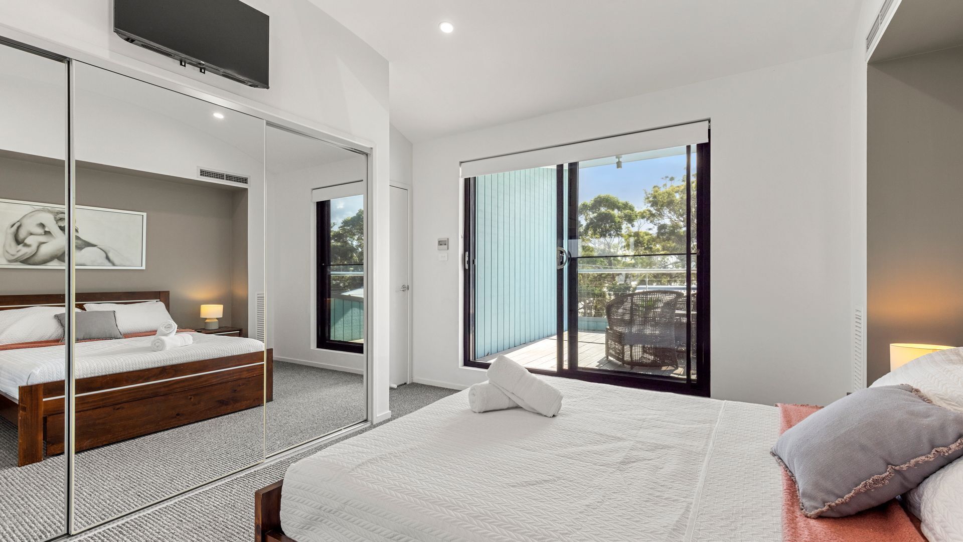 A modern hotel room with a large bed, a glass door leading to an outdoor area, and a flat-screen TV mounted on the wall.