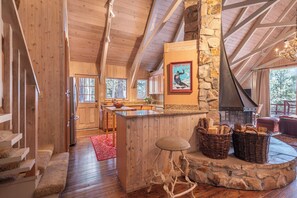 A wooden interior with a stone fireplace, a kitchen area, and a dining space.