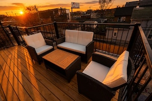 A wooden deck with wicker furniture and a view of the sunset.