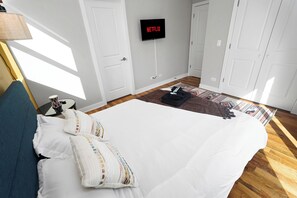 Un dormitorio con cama, almohadas, un televisor montado en la pared y un tapete estampado en el suelo.