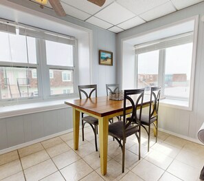 A dining area with a wooden table and chairs, large windows, and a view of buildings outside. - IR20 Walk to Sandfest, Shared Pools, Boardwalk to Beach (Port Aransas)