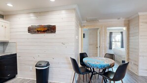 A compact kitchen with a built-in stove, a trash bin, and a dining area with a table and chairs. - Shared Pool, Pet Friendly (Port Aransas)