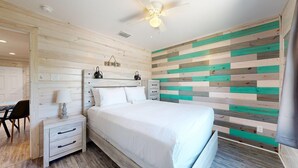 A bedroom with a wooden headboard, a bed, a nightstand, a chair, and a wall with a striped pattern. - Shared Pool, Pet Friendly (Port Aransas)