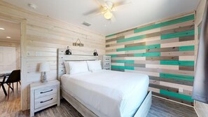 A bedroom with a wooden headboard, a bed, a nightstand, a chair, and a wall with a striped pattern. - Shared Pool, Pet Friendly (Port Aransas)