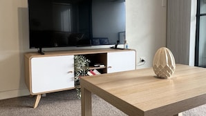 Ett modernt vardagsrum med en platt-TV, ett soffbord i trä och en dekorativ vas.