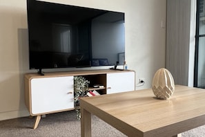 A modern living room with a flat-screen TV, a wooden coffee table, and a decorative vase. - The Beating Heart of Gungahlin (Canberra)