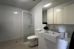 A modern bathroom with a glass-enclosed shower, a toilet, a sink, and a mirror above the sink. - The Beating Heart of Gungahlin (Canberra)
