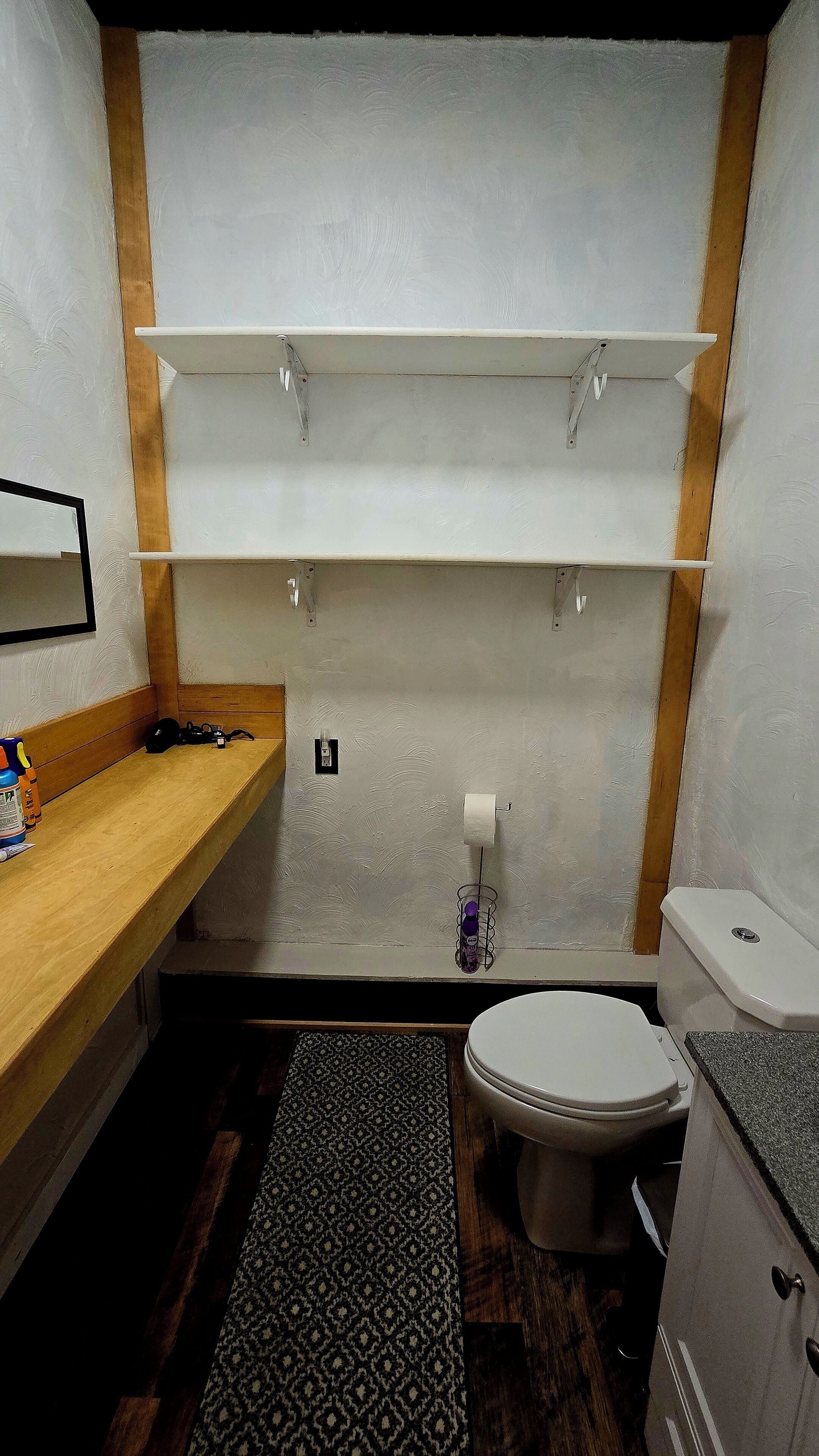 Une salle de bain comprenant des toilettes, un lavabo, un miroir et une étagère au-dessus du lavabo.