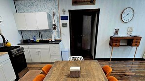 Ein Essbereich mit einem Holztisch, orangefarbenen Kissen und einem weißen Stuhl mit geometrischem Muster.