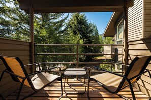 A wooden deck with two chairs and a small table, overlooking a forested area. - Park City Red Pine Mountain Haus – 4BR/4BA, Pool & Hot Tubs (Park City)