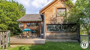 A wooden cabin with a deck, large windows, and a covered outdoor seating area. - Le grand gîte de Combes (BESSE ET SAINT ANASTAISE)