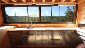 A kitchen with a large window, wooden cabinets, and a sink. - Le grand gîte de Combes (BESSE ET SAINT ANASTAISE)