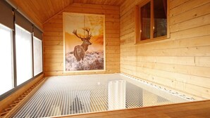 A wooden cabin with a large window, a metal bed frame, and a poster of a deer. - Le grand gîte de Combes (BESSE ET SAINT ANASTAISE)