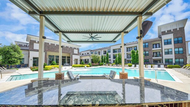 Ein Poolbereich auf dem Dach mit überdachter Sitzgelegenheit, einem Pool und modernen Gebäuden im Hintergrund.