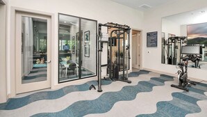 Ein Fitnessstudio mit Trainingsgeräten, einer Spiegelwand und einem gemusterten Teppich.