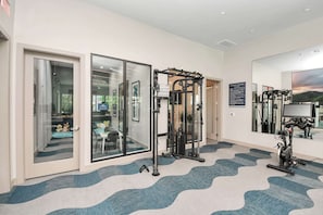 A fitness center with exercise equipment, a mirrored wall, and a patterned carpet.