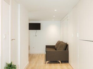 Un salon moderne avec un canapé, un téléviseur à écran plat fixé au mur et une petite plante.