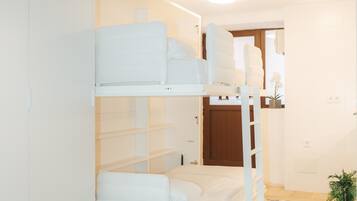 A bunk bed room with white bedding, a small plant, and a checkered floor.