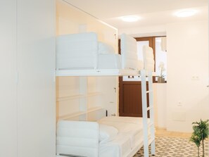 Une chambre avec un lit superposé, une literie blanche, une petite plante et un sol à carreaux.