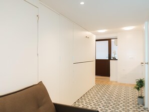 Un pasillo con piso estampado, un sofá marrón y una puerta que da a una habitación con ventana.