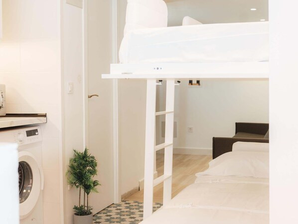 Une pièce avec un lit superposé, un lave-linge, une petite plante en pot et un sol à carreaux.
