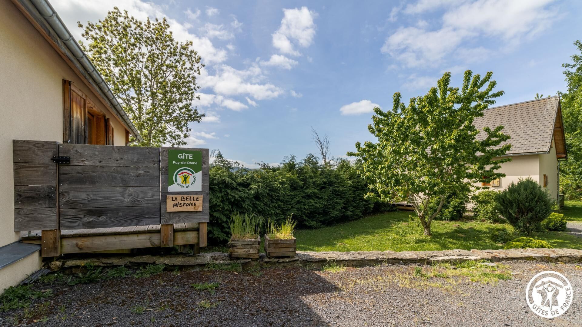 A rustic building with a wooden gate, a signboard for GITE Puy-de-Dome, and a well-maintained garden.