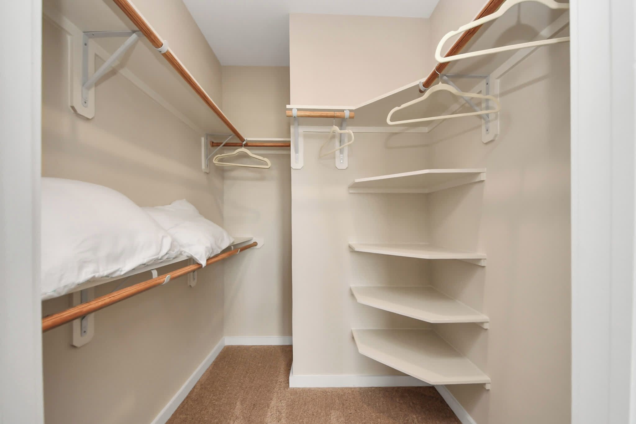 Ein kleiner, schmaler Raum mit einem Etagenbett, einem Holzbodenregal und einem weißen Kleiderschrank mit Kleiderstange.
