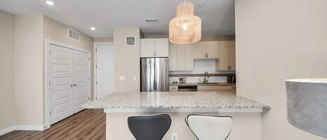 A modern kitchen with granite countertops, stainless steel appliances, and a hanging pendant light.