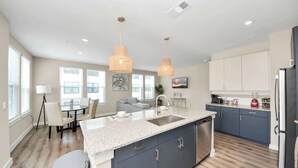 A modern kitchen with a granite countertop, dark cabinets, a stainless steel sink, and pendant lighting. - Luxurious 2BR King Beds  Apartment in Montgomery with Pool, Gym & Game Room (Montgomery)