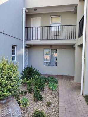 A two-story building with a balcony, a door marked '58', and a small garden area with various plants. - The Apartment and Estate (Cape Town)
