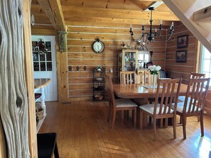 A wooden dining room with a wooden table, chairs, a chandelier, a clock, and a window.