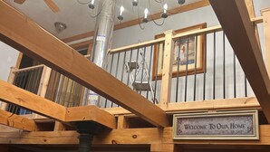 Interior em madeira com um candelabro, uma placa com a mensagem 'Welcome To Our Home' e uma lareira.
