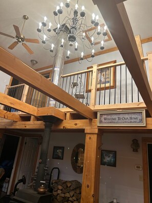 A wooden interior with a chandelier, a 'Welcome To Our Home' sign, and a fireplace.