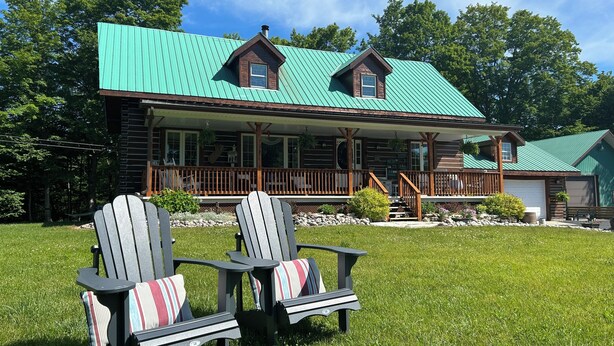 Uma cabana de tronco com varanda, duas cadeiras Adirondack e um telhado de metal verde.